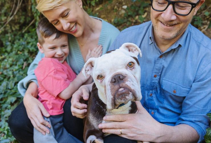 Bulldog surrounded by a loving family outside in front of some folliage