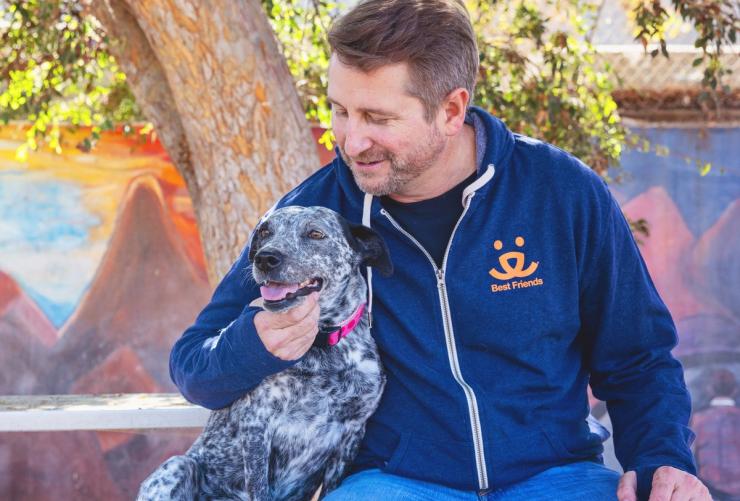 Smiling person wearing a Best Friends sweatshirt sitting with a dog outside