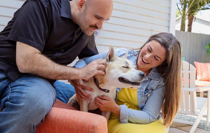 Smiling people relaxing on a patio chair with a dog between them