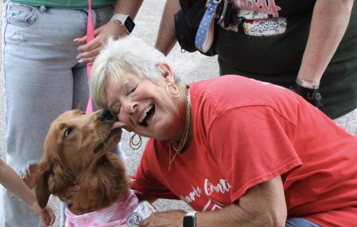 Smiling person being kissed by a brown dog wearing a bandanna