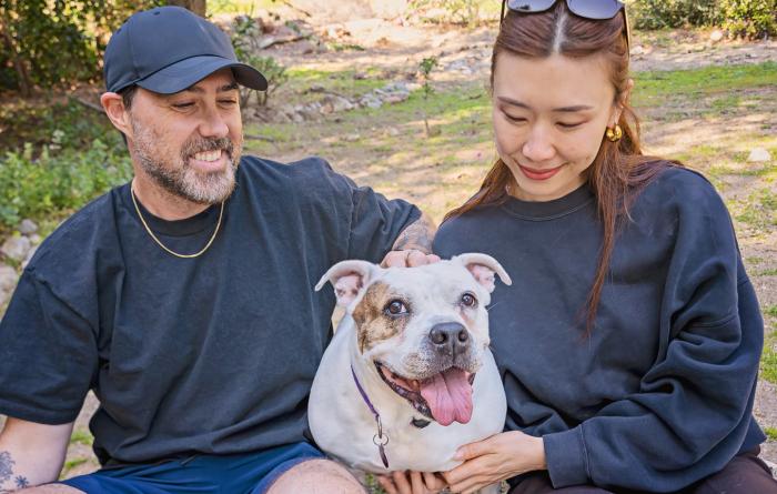Two people petting Coconut, ahappy dog who is smiling