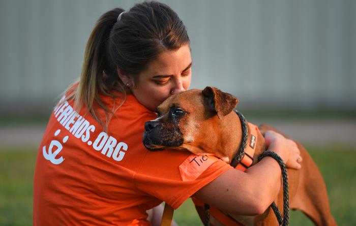 Person wearing orange Best Friends T-shirt hugging a dog