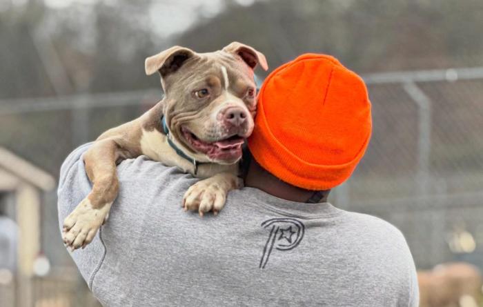 Person wearing a read hat holding a dog over his shoulder