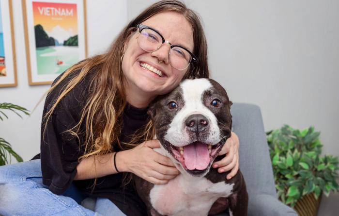 Smiling person sitting in a chair hugging a black and white dog