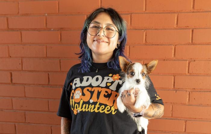 Person wearing an Adopt Foster Volunteer Best Friends T-shirt holding a small puppy