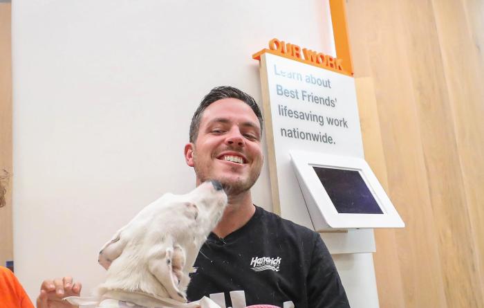 Alex Bowman smiling and getting kissed on the face by a large white dog