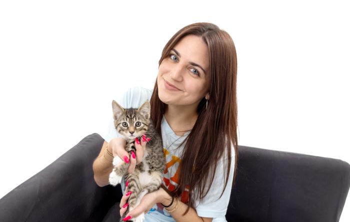 Smiling person sitting on a couch holding a tabby kitten