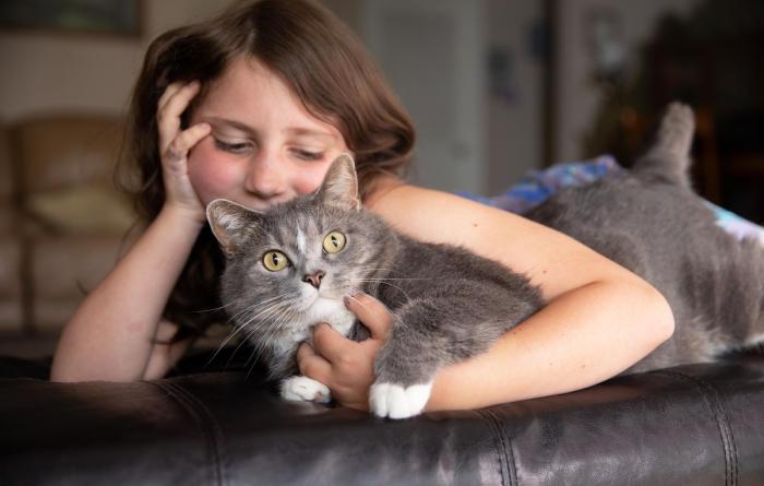 Young person lying down and hugging a gray and white cat