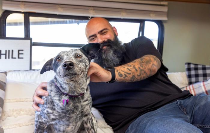 Smiling man sitting next to and petting a happy black and white spotted dog