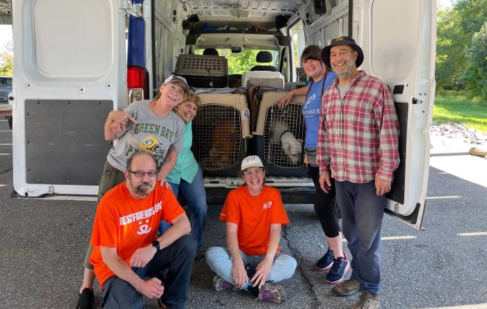 Six smiling people at the back of a van with the back doors open, showing multiple animal kennels