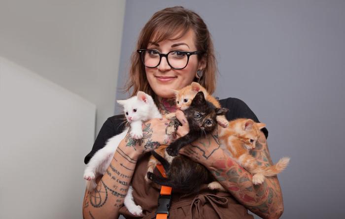 Smiling person holding a litter of kittens