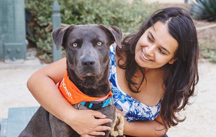 Smiling person outside with a leashed dog wearing a bandanna