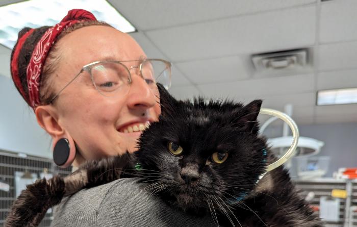Smiling person holding Fossey the cat over her shoulder