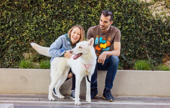 Two smiling people sitting with a dog outside