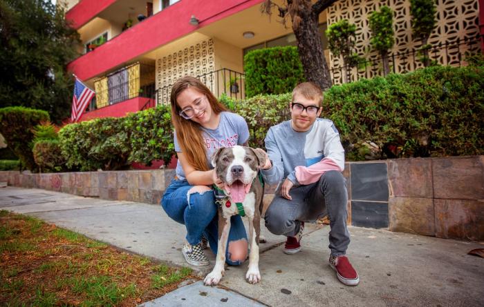A couple and happy pit bull type dog outside in front of a home