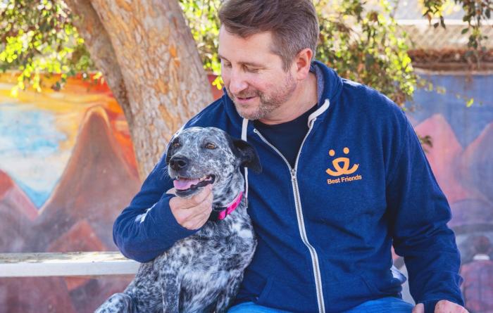 Smiling person wearing a Best Friends sweatshirt sitting with a dog outside