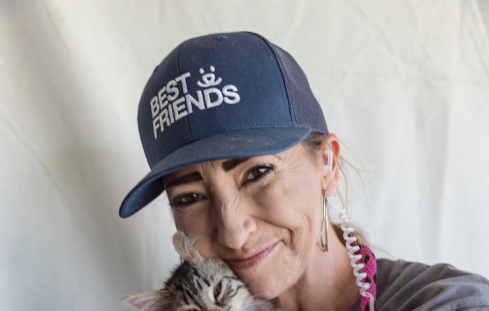 Smiling person wearing a hat cradling a tabby cat