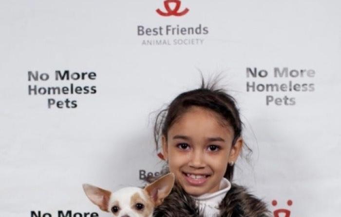 Child holding a Chihuahua in front of a Best Friends No More Homeless Pets backdrop
