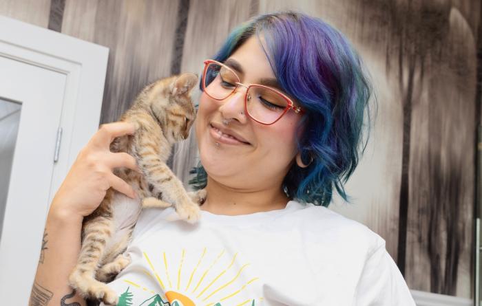Smiling person with multi-colored hair holding a tabby kitten