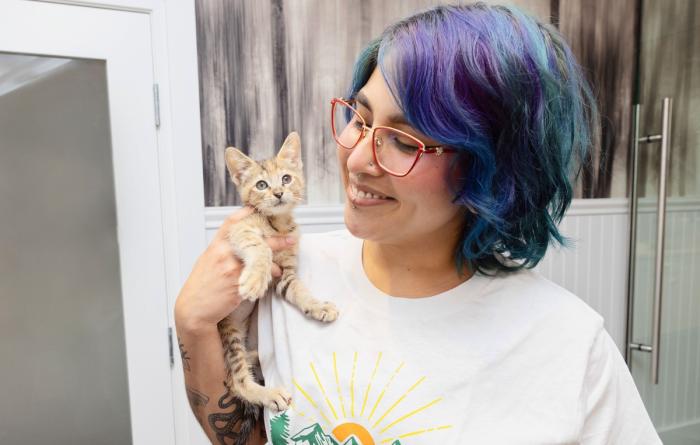 Smiling person with multi-colored hair holding a kitten