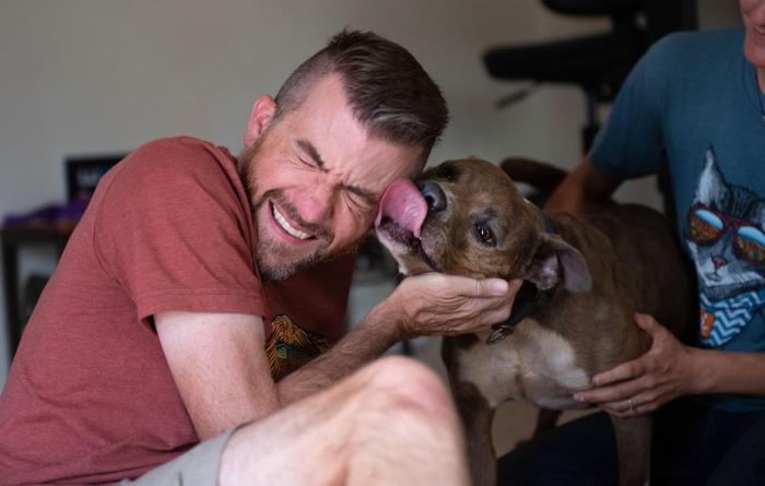 Man smiling and laughing as a dog kisses his face
