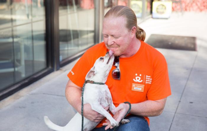 Person wearing a Best Friends orange T-shirt being kissed on the face by a small white dog