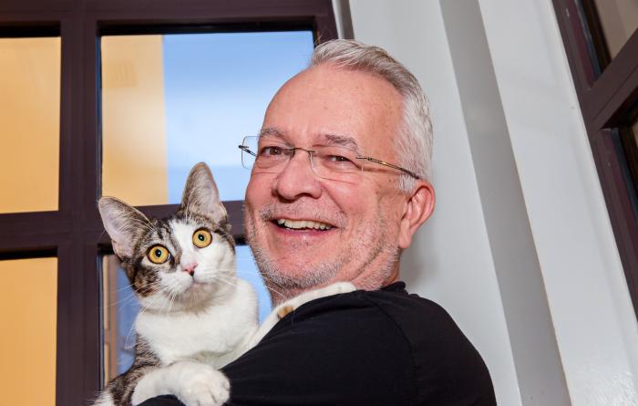 Smiling person holding a white and tabby cat in front of a window