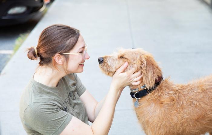 Profile of smiling person who is affectionately holding the head of a tan dog