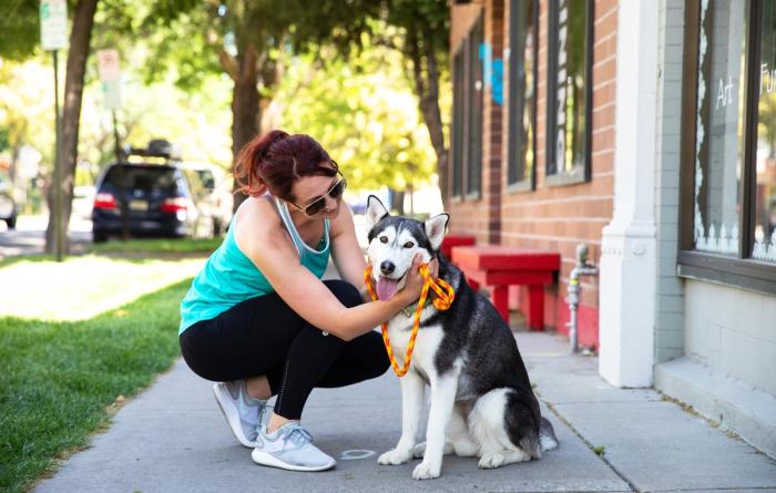 Smiling person kneeling down next to a happy leashed dog on a sidewalk
