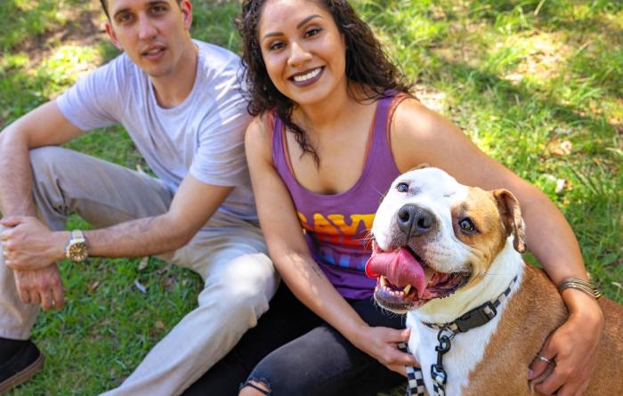 Two smiling people relaxing in the grass with their dog