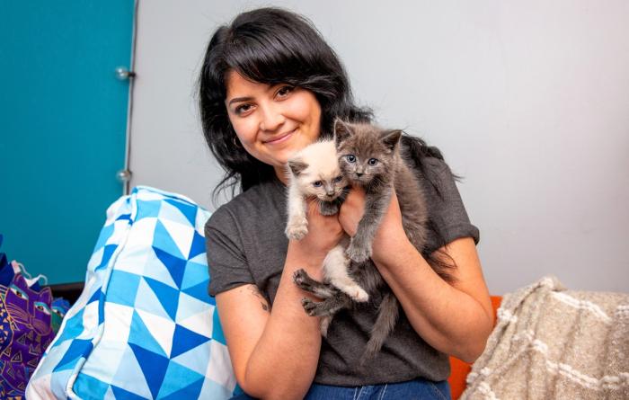 Smiling person holding two tiny kittens