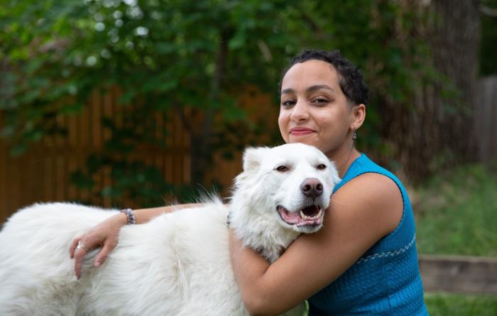 Smiling person hugging a large white dog outside in a fenced area