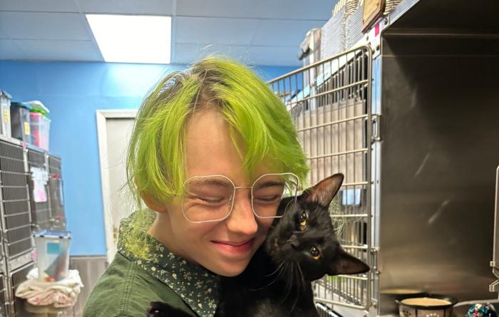 Person cuddling with a black cat outside of some kennels