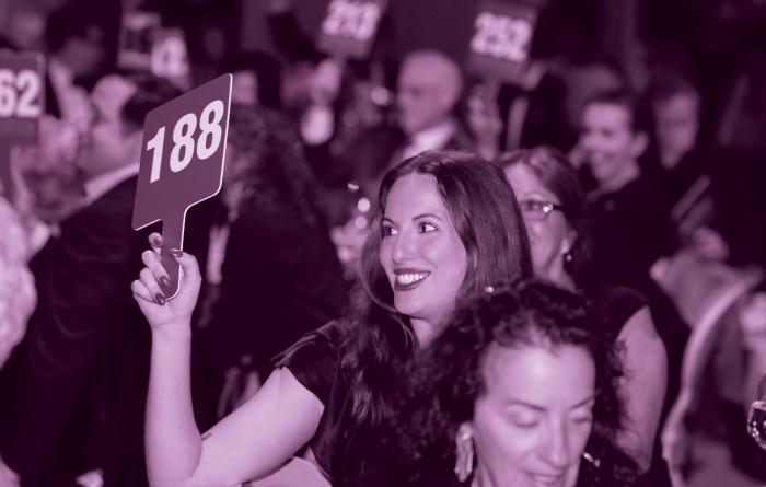 Smiling person holding a bidding number for an auction