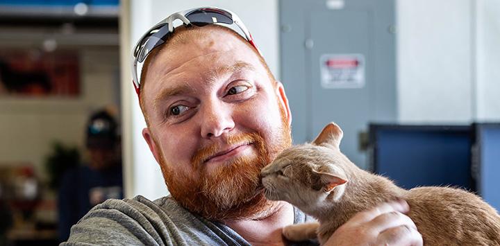 Bearded man holding a cat who is kissing his chin