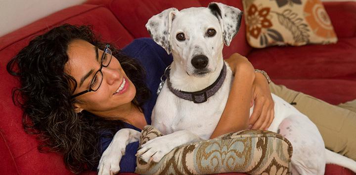 Woman lying on the couch with a white and black dog who she's hugging