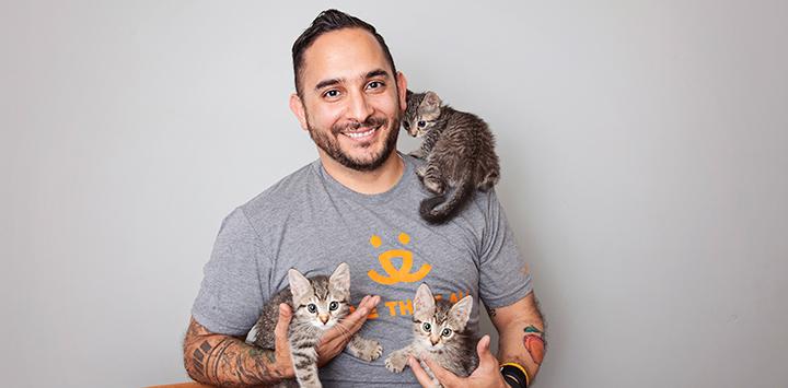 Marc Peralta holding two kittens and with a third kitten on his shoulder