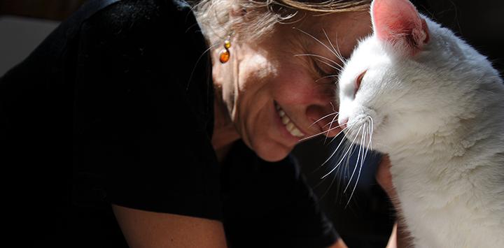 Smiling woman with her head against the head of a white cat