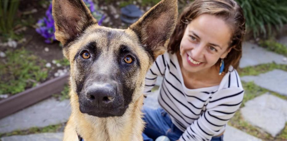 Smiling person sitting outside with a dog on a stone patio
