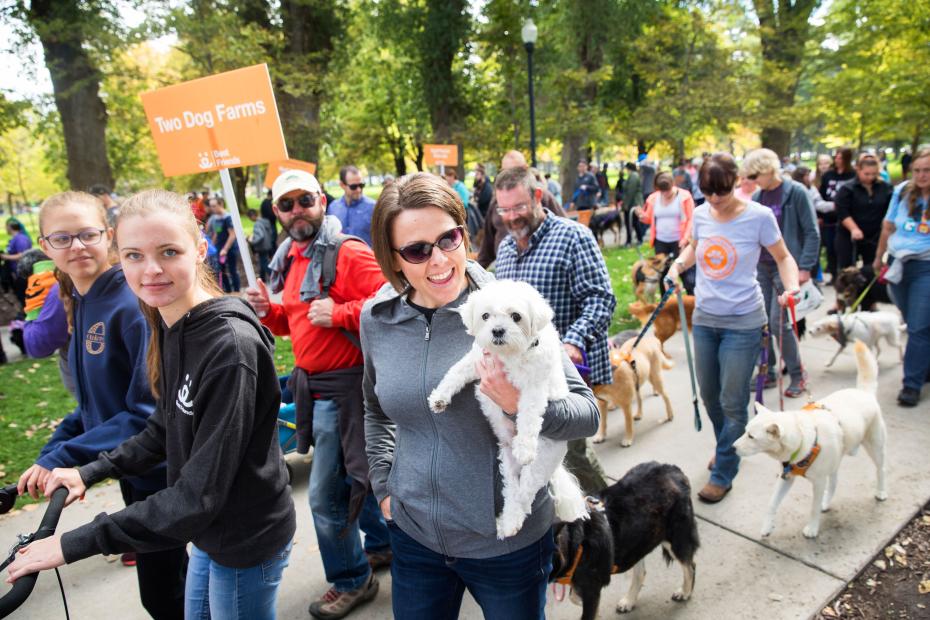 Group of people walking during a Strut Your Mutt event, with one smiling person holding a small white dog in the foreground