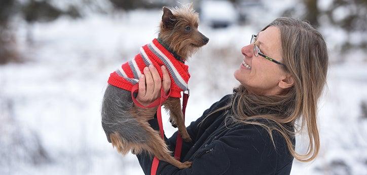 Woman holding a terrier dog wearing a red sweater