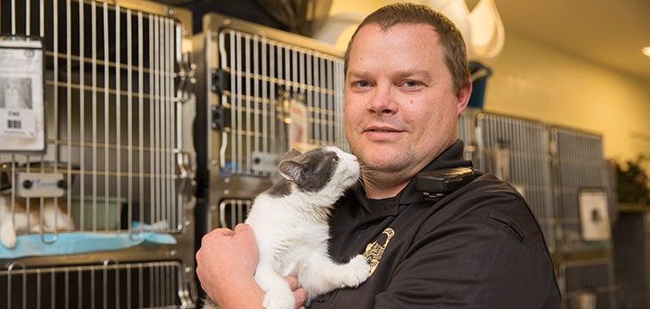 Animal control officer holding a cat in front of some kennels at a municipal shelter