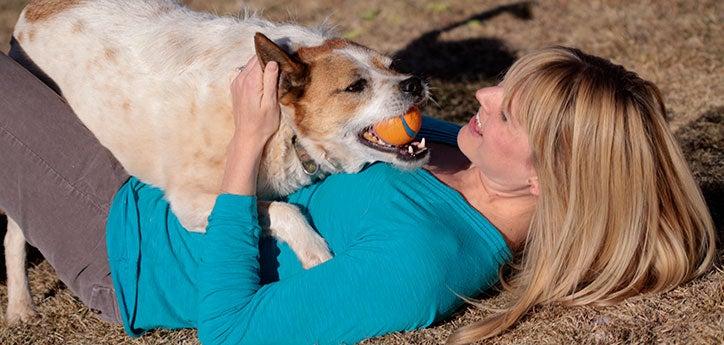 Woman and her dog with ball. She is keeping him safe by supervising his play time.