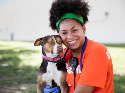 Smiling person wearing a Best Friends orange T-shirt hugging a dog outside