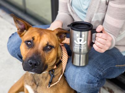 Person holding a Best Friends travel mug while sitting with a dog outside