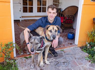 Smiling person sitting on a step outside with two big dogs