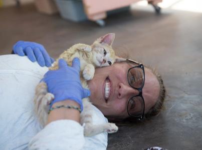 Woman in scrubs lying on the floor with a kitten.
