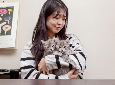 Woman smiling holding two kittens.