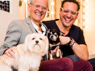 Two smiling people sitting on a couch with two small dogs