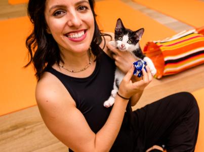 Smiling person holding a kitten while sitting on a yoga mat